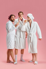 Three men, friends in bathrobes and slippers drinking champagne, celebrating and having fun against...