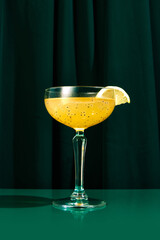 Close up photo of exotic alcohol drink in tall glass with wide mouth garnished with piece of orange sitting on green table. Concept of party time, restaurant, holidays, Valentines Day, celebration