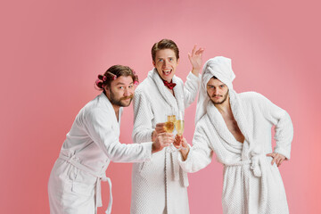 Happy New Year. Positive young men, friends in bathrobes after shower, clinking champagne glasses...