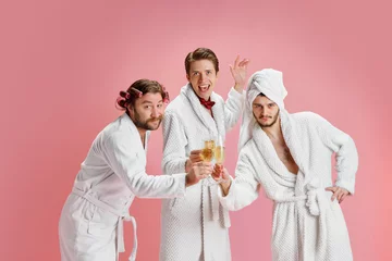 Photo sur Plexiglas Spa Happy New Year. Positive young men, friends in bathrobes after shower, clinking champagne glasses against pink background. Concept of leisure activity, fun, bachelor party, friendship, spa