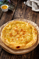 Golden-browned Megrelian khachapuri on parchment, with a rustic wooden backdrop, inviting and traditional