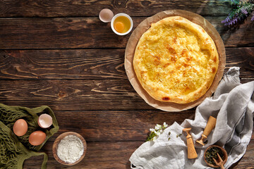 Megrelian-style khachapuri on textured wood, with eggs and flour, under natural light, rustic Georgian charm