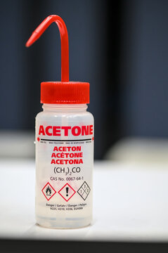 Acetone wash bottle, with red beak. Different translations, chemical pictograms and formulations are indicated on the bottle body.