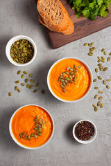 Pumpkin soup with seeds, spices, pepper, herbs and bread on a gray background, shot from above. The concept of healthy vegetable soups. Concept of healthy eating