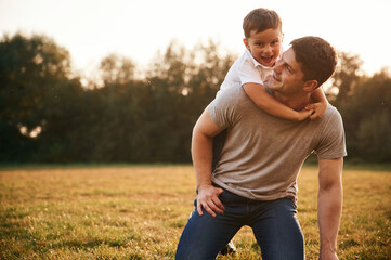 Embracing dad from behind. Father and little son are playing and having fun outdoors - obrazy, fototapety, plakaty