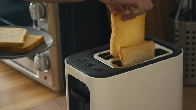 High angle stab side shot of male hands holding plate and loading two slices of white bread into toaster whilst preparing breakfast in modern kitchen