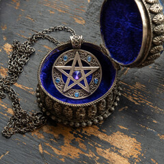 Pentagram star pendant with blue crystals lies in a metal box with blue velvet on old black painted...