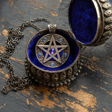 Pentagram star pendant with blue crystals lies in a metal box with blue velvet on old black painted worn wood