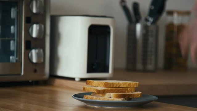 Midsection side shot of unrecognizable man taking two slices of white bread from toaster and placing them on plate then going away in modern kitchen