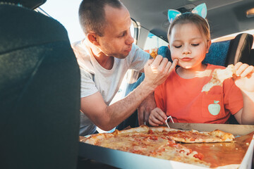 Father wiping gently daughter's mouth while eating just cooked Italian pizza during family car trip...
