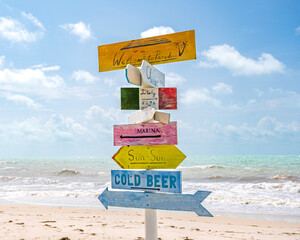 A colourful, wooden signpost, on a tropical beach, against a blue, summer sky - obrazy, fototapety, plakaty