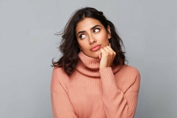 Captivating young Arab woman in winter fashion, isolated background, displaying a thoughtful and graceful pose with hand gently resting on her chin - obrazy, fototapety, plakaty