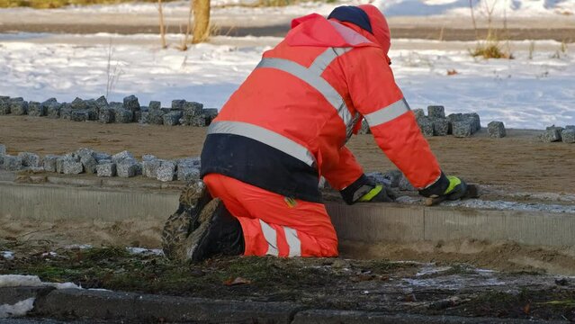 Roadworks Construction Worker in Protective Safety Workwear Laying Paving Bricks on Pedestrian Sidewalk on Cold Winter Day