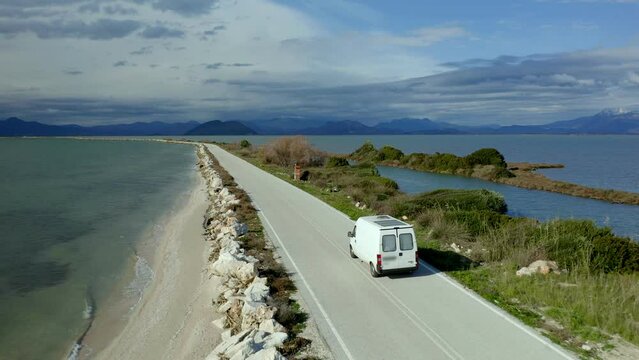 Drone aerial view of camper van with solar panels driving in Koronisia road in the middle of the sea, in Greece