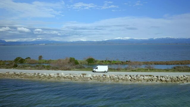Drone aerial view of camper van with solar panels driving in Koronisia road in the middle of the sea, in Greece