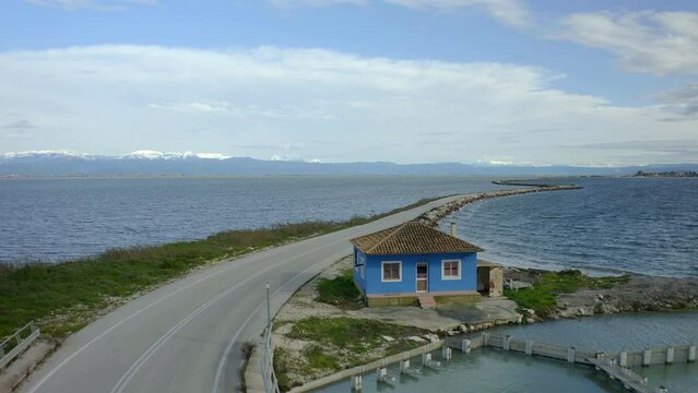 Drone aerial view of traditional greek blue house in Koronisia famous road in the middle of the sea with mountains in the background