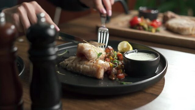 Perch fillet with vegetables and sauce. Woman eats delicious and healthy food sitting at the table, close-up. Lunch in a restaurant. Restaurant menu with different dishes