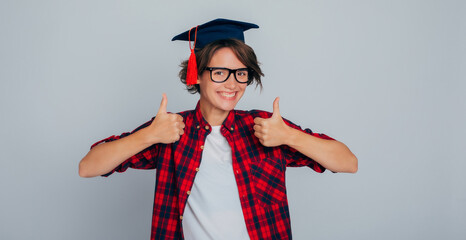 Portrait of happy and joyful university graduate in glasses and graduation cap with thumbs up....