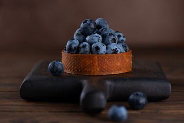 Dessert tartlet with blueberries and cream, fresh dessert for breakfast on a wooden board.