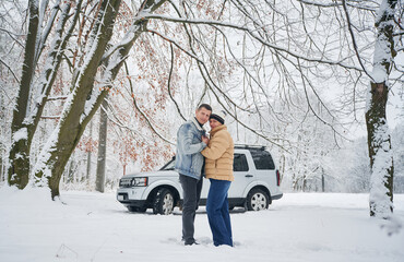 Standing and posing. Beautiful couple are near the car in the winter forest