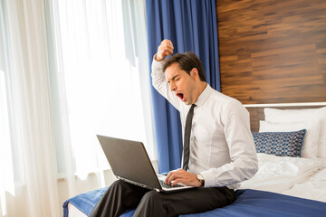 Tired businessman in suit working on the hotel bed on his computer laptop notebook
