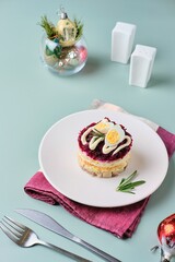 Portioned herring salad under a fur coat, herring under layers of boiled vegetables, eggs, smeared with mayonnaise, on a white plate on a green plain background.
