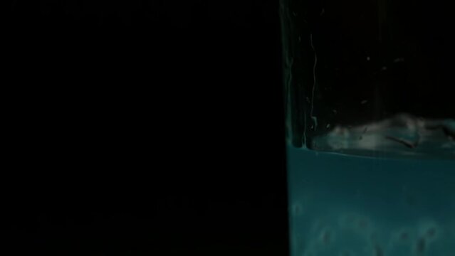 Turquoise cocktail is poured into a glass on a black background on the right