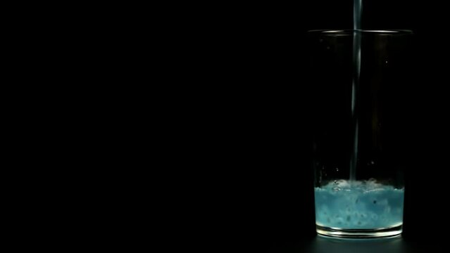 Turquoise cocktail is poured into a glass on a black background