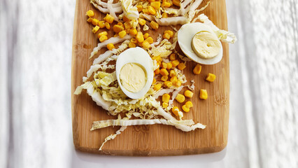 Chopped Peking cabbage, peeled eggs and yellow canned corn on cutting board as a background....