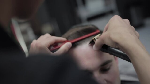 Hair clipper cutting the head of a handsome caucasian male client in a hair salon, close-up. Modern and stylish haircuts in the barbershop. Slow motion