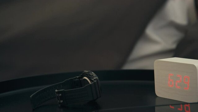Side stab closeup of man taking watch from nightstand checking time and then going back to sleep at home