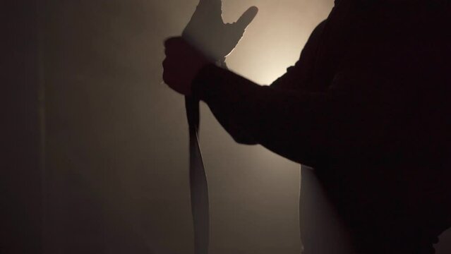 Cropped view of boxer wrapping his hands with white bandages in dark smoke background.
