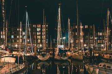 The Hague, Netherlands - January 1, 2020: Scenic panorama of Scheveningen harbour. Romantic modern seaside resort. Brown brick buildings, light windows, moored white yachts and sailboats in evening.