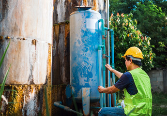Asian man engineer controlling the quality of water places operating industrial water purification or filtration equipment old cement tanks for keeping water in water factory - obrazy, fototapety, plakaty