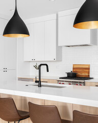 A kitchen detail with white and white oak cabinets, leather chairs sitting at an island, and a...