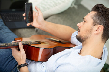 handsome young man holding phone and playing guitar