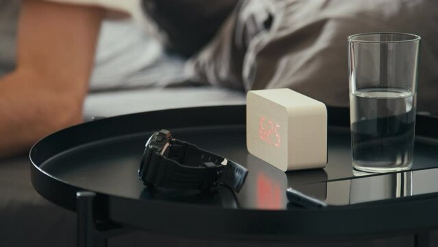 Side stab footage of unrecognizable man waking up in morning at 6 25 am with alarm clock and getting up at home