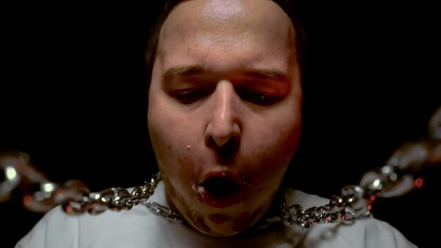 Obesity concept, overeating. Fat plump guy eats burger, fast food. Junk food. Poor and unhealthy nutrition diet. Guy's neck is wrapped in a chain. Close up head. Mayonnaise on lips