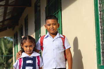 A young Filipino boy with his younger sister. Two students behind a classroom.