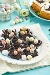Easter chocolate nest cake with mini chocolate candy eggs with blossoming cherry or apple flowers on blue background table. Creative recipe for Easter table with holiday decorations. Top view.