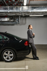 handsome red haired businessman in smart suit leaning on his car and looking away on parking lot