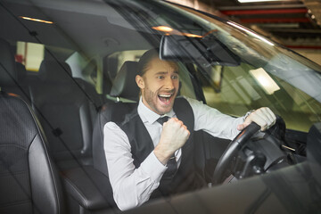 joyous bearded professional in black vest cheering behind steering wheel, business concept