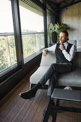 good looking elegant businessman with ponytail in stylish smart black vest sitting on couch