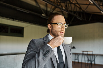 handsome refined professional with glasses and ponytail in smart suit drinking tea and looking away
