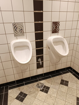 Zwei Urinale auf einer Männertoilette mit Bewegungsmelder und Wasserstelle für Wischeimer.