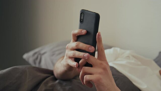 Side stab shot of unplugging charger connection from phone while using it lying in bed in morning at home