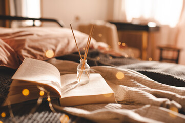 Home liquid fragrance in glass bottle with bamboo sticks on paper book in bed over glow lights...