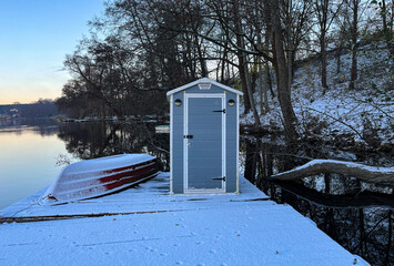 Lake in winter. Boat and equipment house. Reflections in the water. Snow on the shore.
