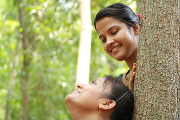 Portrait of Two young Indian Rural girls behind the tree in park.