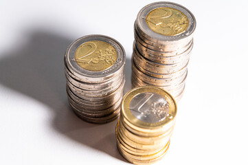 Stacks of coins next to each other, on white surface, and their shadows. Quantity of money, currency and wealth.